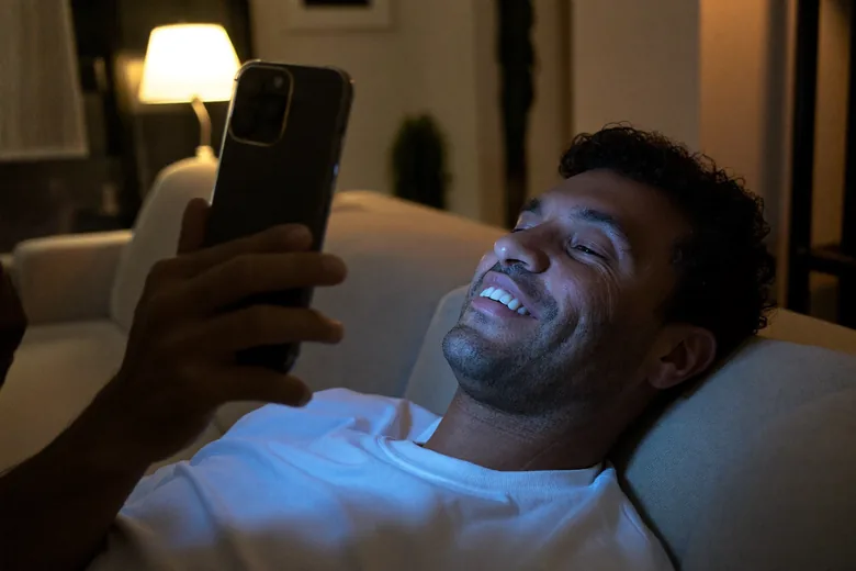 Cliente deitado no sofá, à noite, sorrindo para a resposta que acabou de chegar no celular