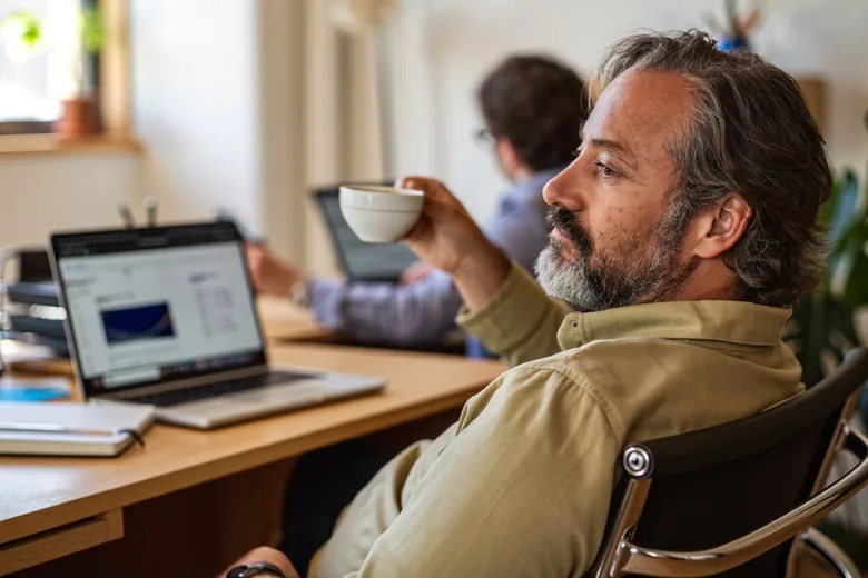 Dono de empresa tranquilo no escritório, com o time trabalhando ao fundo